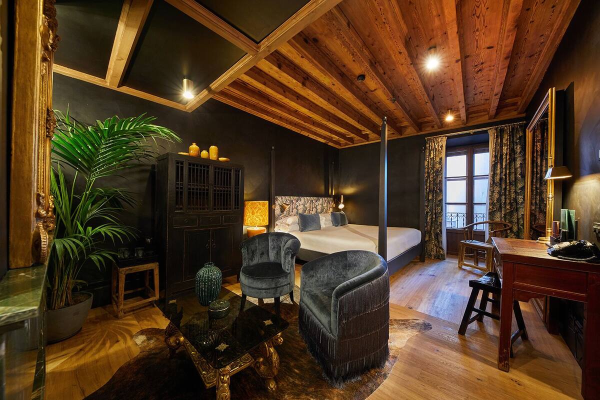 Une chambre confortable avec un lit, deux fauteuils, un bureau et une grande plante.