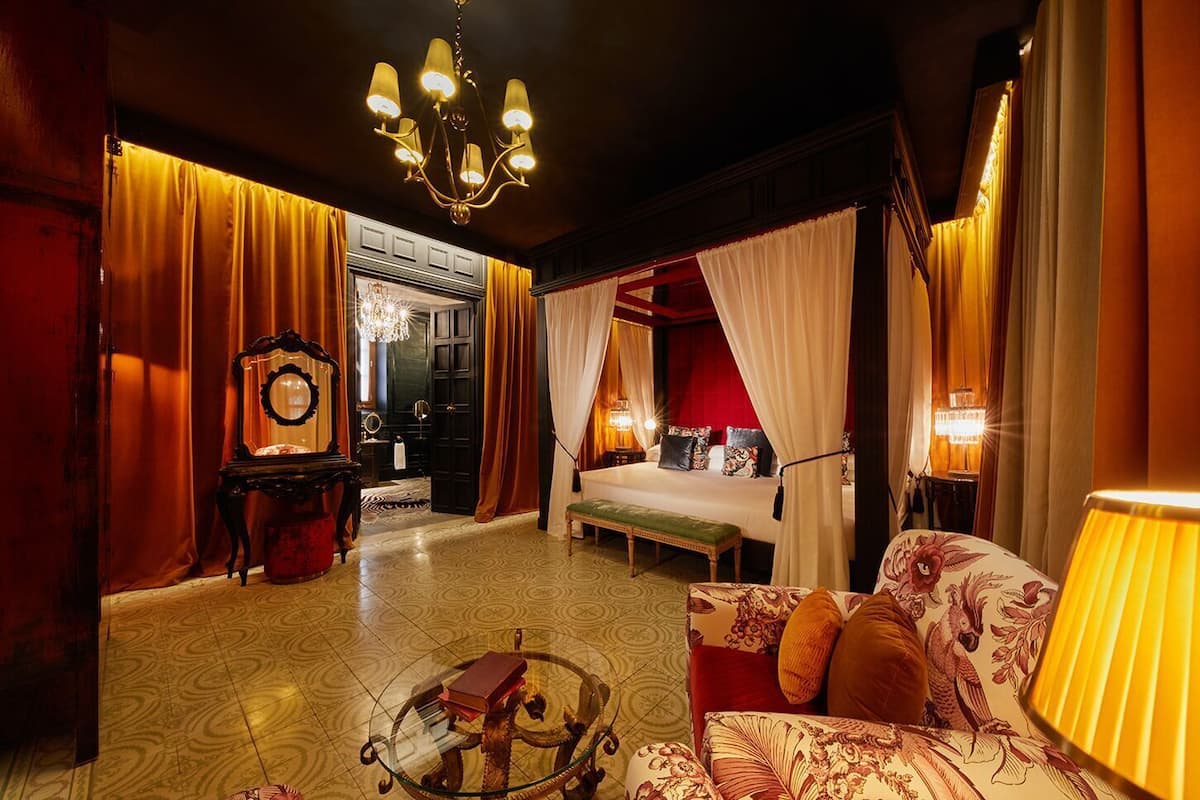 Une chambre à coucher luxueuse, dotée d’un grand lit, d’un coin salon avec un canapé et un fauteuil, d’une table basse en verre et d’un lustre.