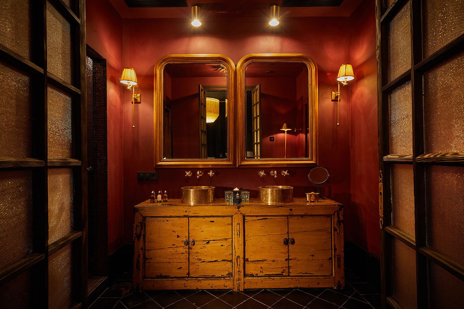 Un baño de estilo vintage con un tocador de madera, dos espejos grandes y apliques de pared.