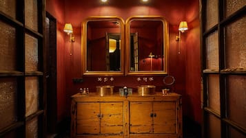 Un baño de estilo vintage con un tocador de madera, dos espejos grandes y apliques de pared.