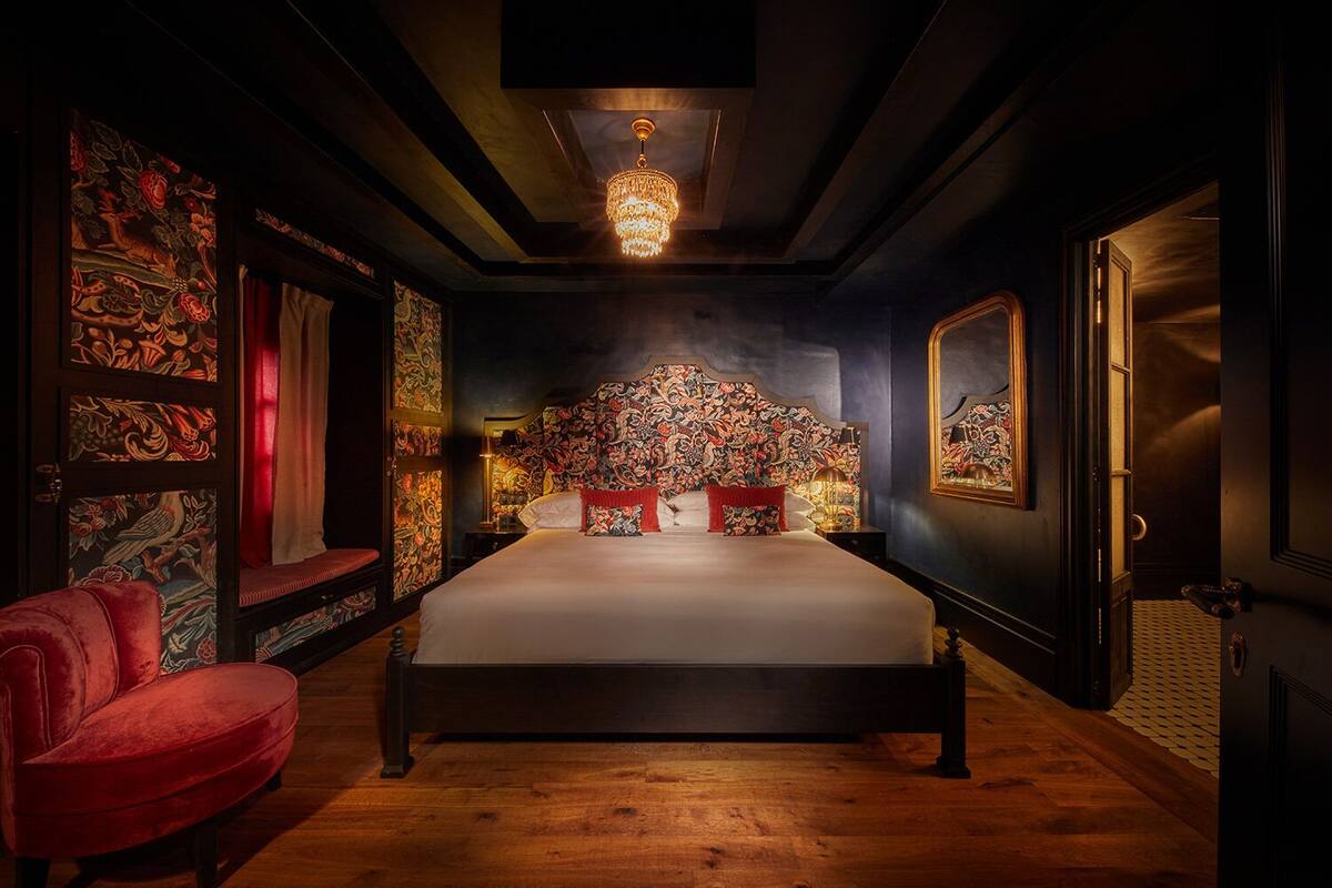 Une chambre avec un grand lit, un fauteuil rouge et un lustre.