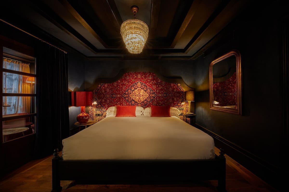 Un grand lit avec une tête de lit rouge, un lustre et un miroir au mur.