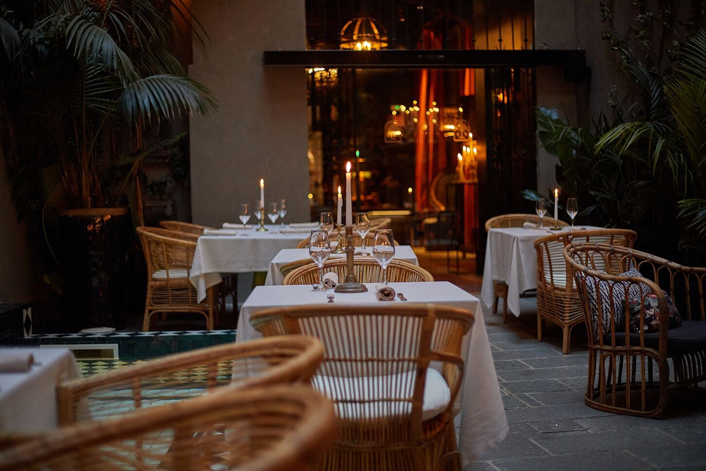 Restaurante com cadeiras e mesas de vime, velas e ambiente acolhedor.
