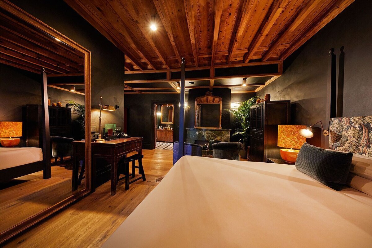 A room with a bed, a desk, a chair, a mirror, and a fireplace.