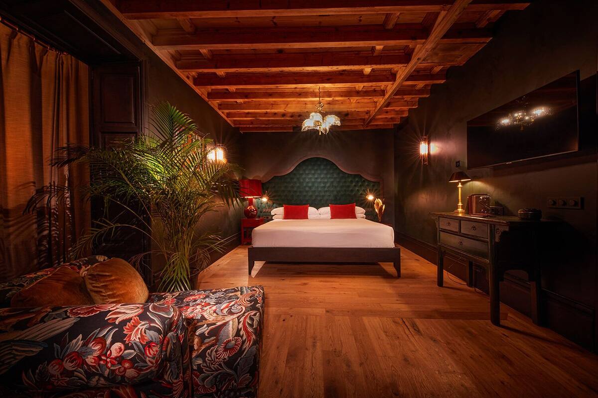 Une chambre avec un plafond en bois, un lit avec une literie rouge et blanche, une grande plante et un bureau avec une lampe.