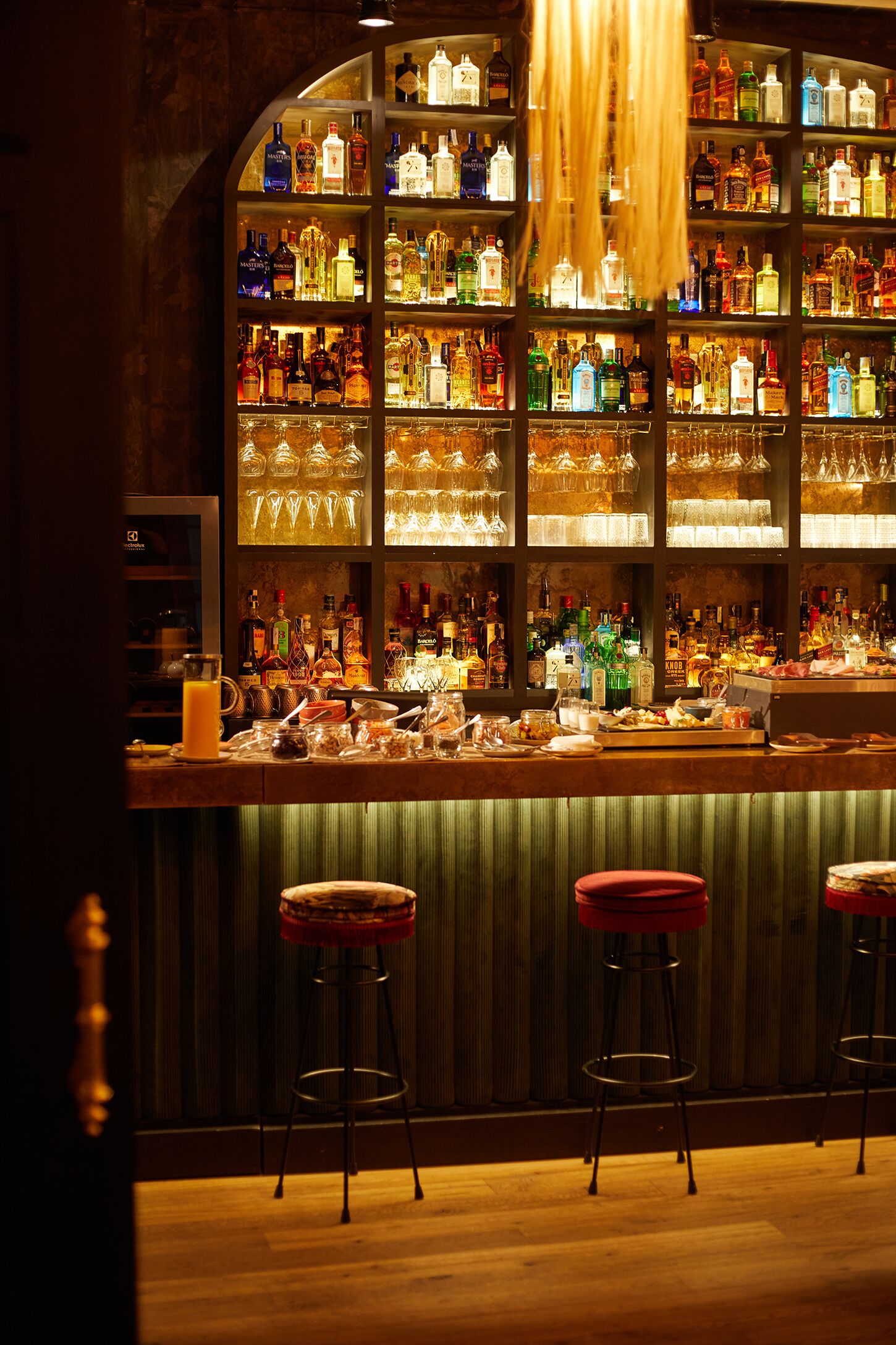 A bar area with shelves of liquor bottles, glasses, and stools.