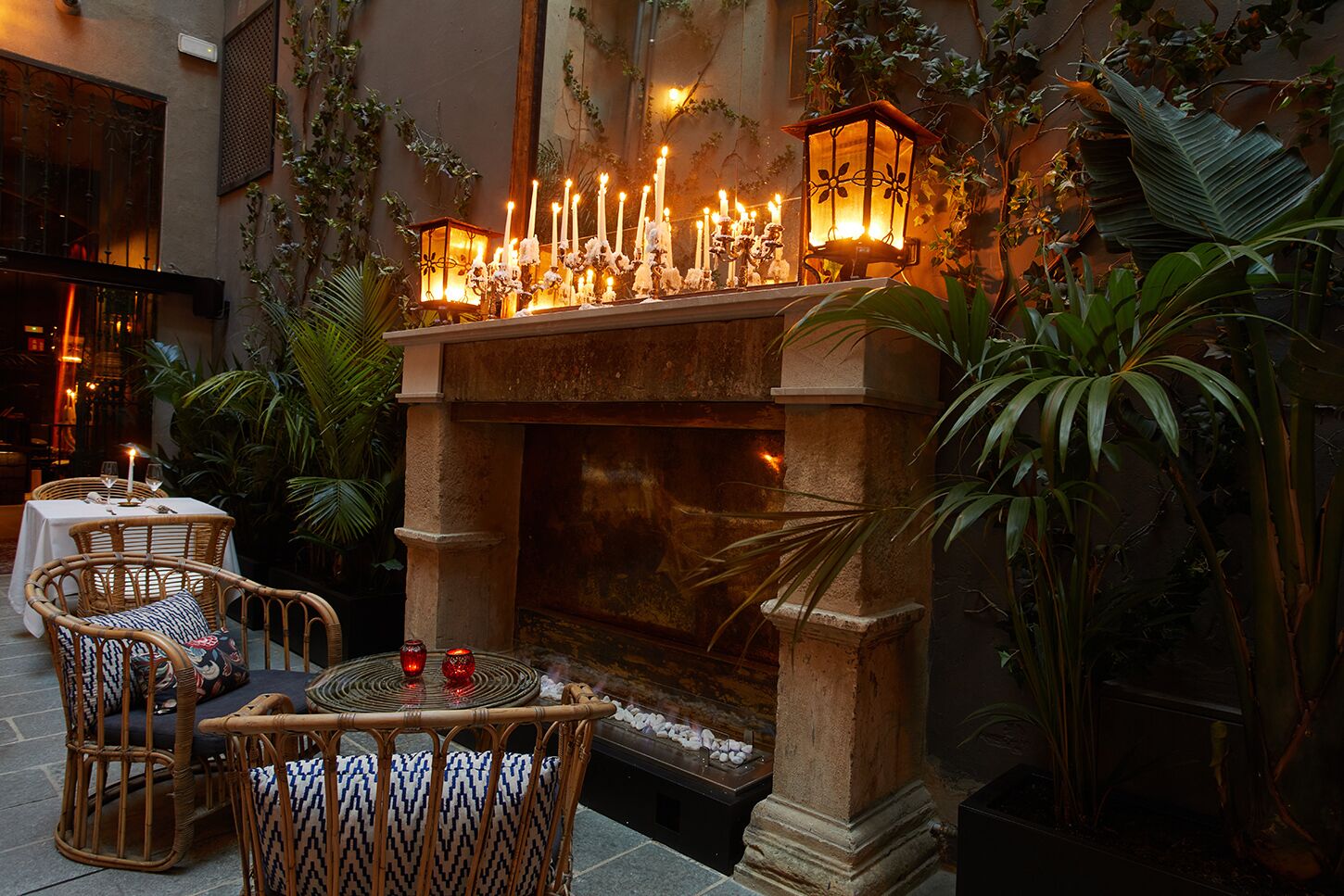 Un patio al aire libre con una chimenea de piedra, mobiliario de mimbre y plantas en macetas.