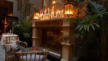 Un patio al aire libre con una chimenea de piedra, mobiliario de mimbre y plantas en macetas.