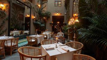 Un comedor interior con sillas y mesas de mimbre, rodeado de plantas e iluminación cálida.