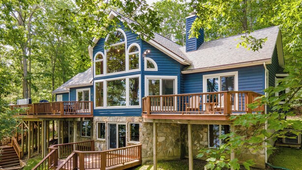 A two-story house with a stone foundation, wooden deck, and a staircase leading to the upper level.