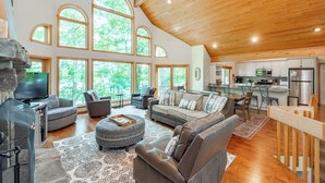 A spacious living area with a high ceiling, large windows, and a modern kitchen.