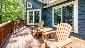A wooden deck with Adirondack chairs and a table, surrounded by a blue house with large windows.