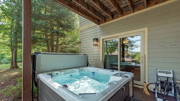 Un jacuzzi en una terraza de madera con un cerramiento de vidrio que da a un porche cubierto.
