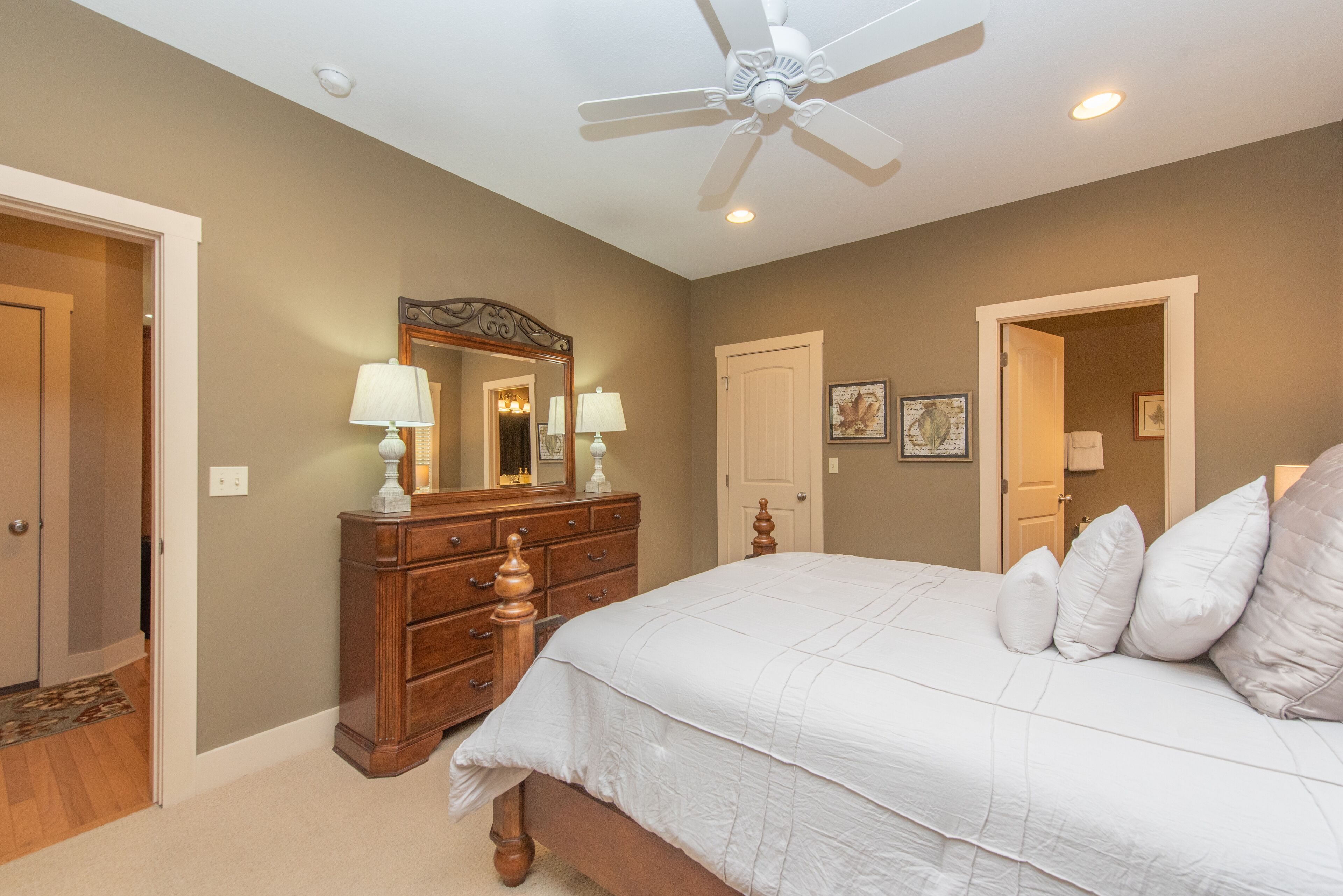 A bedroom with a bed, dresser, mirror, ceiling fan, and two doors.
