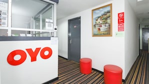 A hotel corridor with a reception desk, a painting of a lakeside scene, and red stools. - OYO 90345 TM Hotel (Taman Melawati)