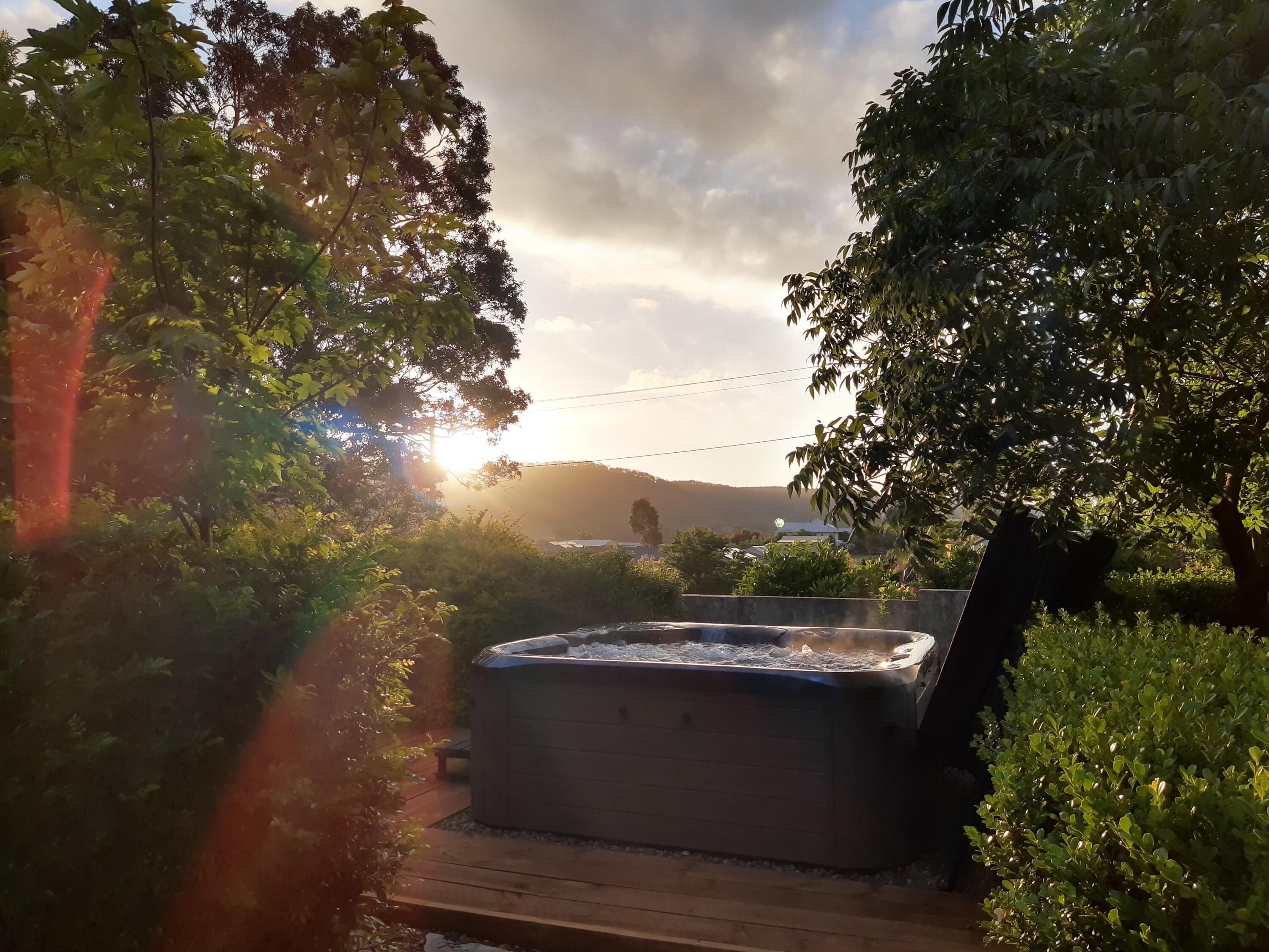 Ein Whirlpool in einem Garten mit Bäumen und Sonnenuntergang im Hintergrund.