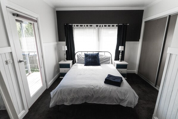 A bedroom with a large bed, two bedside tables, a window with curtains, and a door leading outside.