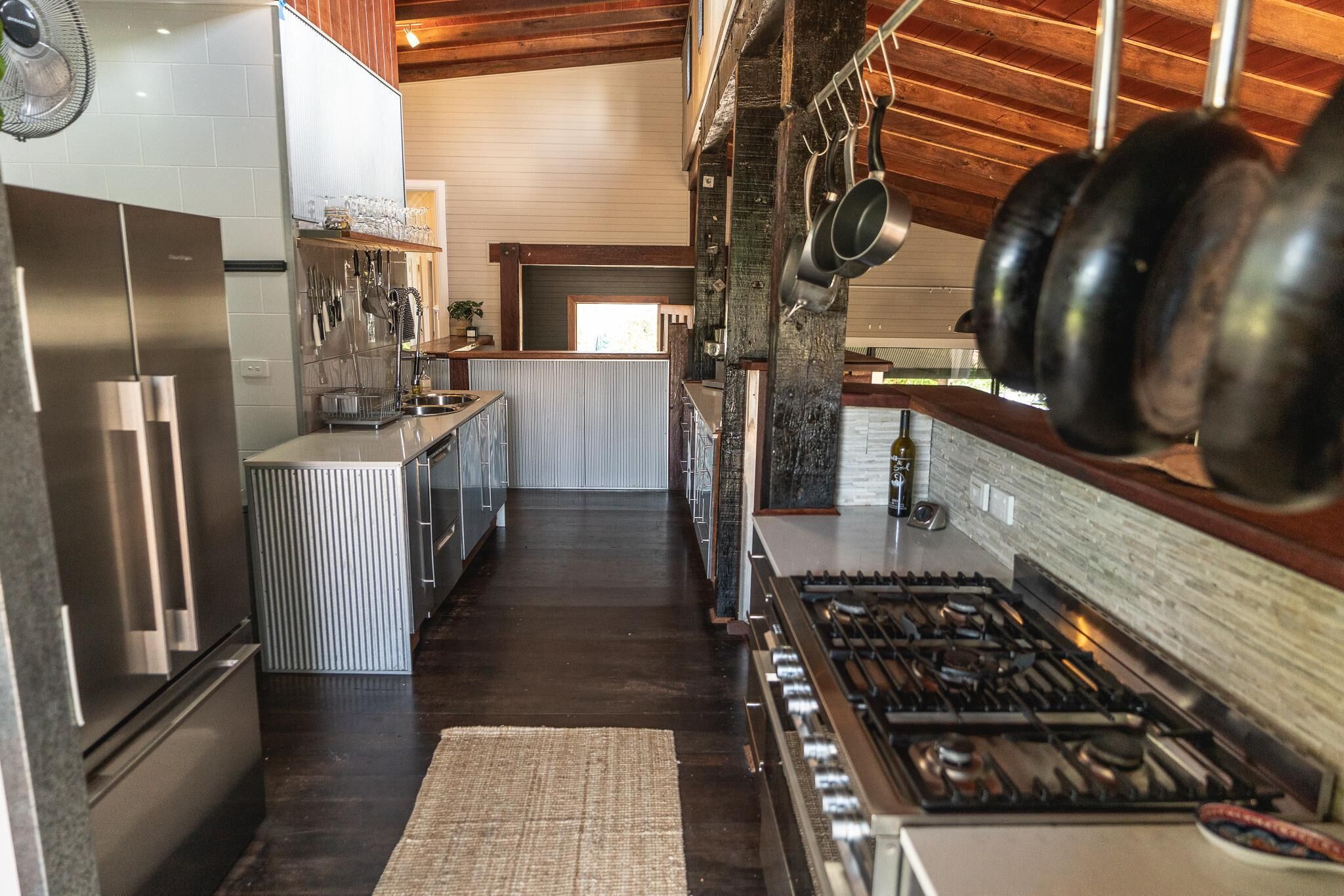A modern kitchen with stainless steel appliances, a central island, hanging pots, and a view to the dining area.