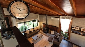 A spacious living area with a large clock, wooden ceiling, and a cozy fireplace.