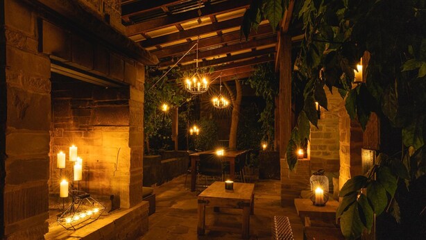 An outdoor patio with stone flooring, wooden furniture, and hanging lights.