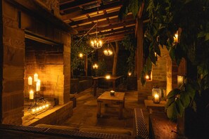 An outdoor patio with stone flooring, wooden furniture, and hanging lights.