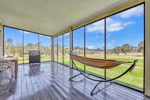 A covered outdoor area with a hammock, a grill, and a view of a lake and trees.