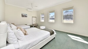 A hotel room with a large bed, two bedside tables, a ceiling fan, and three windows with views of the outdoors.
