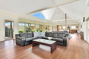 Amplia sala de estar con un sofá modular grande, una mesa de centro y vistas al exterior a través de amplios ventanales.