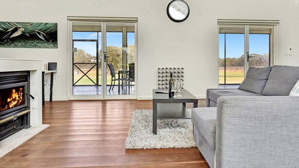 A living room with a fireplace, a sofa, a coffee table, and a view of the outdoors through large windows.