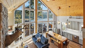 A spacious living area with a large window overlooking a lake, a cozy seating area, and a wooden dining table.