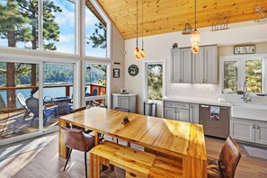 A modern kitchen with large windows, a wooden dining table, and a view of the outdoors.