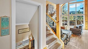 A spacious living area with a wooden staircase, large windows offering a view of the outdoors, and a sign indicating the property is in Lake Tahoe, California.