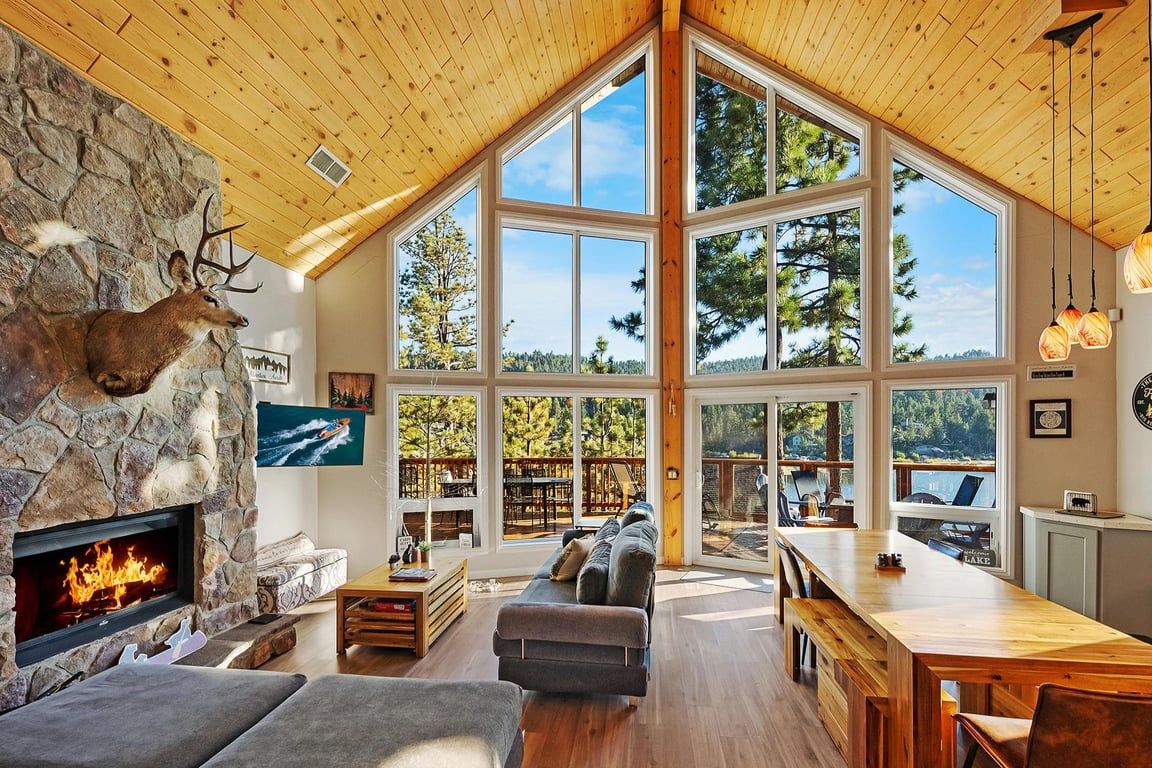 A spacious living area with a stone fireplace, a large wooden dining table, and a view of the outdoors through expansive windows.