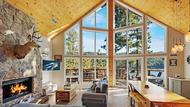 A spacious living area with a stone fireplace, large windows, and a high ceiling.