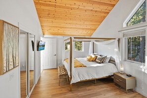Un dormitorio con cama con dosel, una mesita de noche, un banco y un televisor en la pared.
