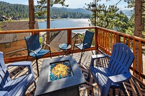 A deck with outdoor seating, a fire pit, and a view of a lake and forest. - Window Wonderland by Destination Big Bear : Custom Luxury Built Near the Lake! Breathtaking Lake Views! Gameroom! Hot Tub! (Big Bear Lake)