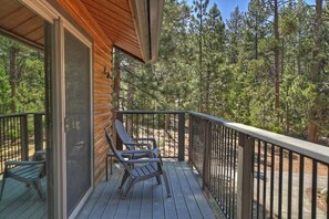 A wooden deck with two Adirondack chairs, a glass door, and a view of a forest.