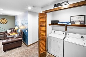 A laundry area with a wooden door, two white washing machines, and a shelf with a framed picture.