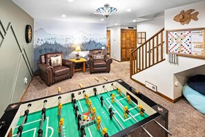 A room with a foosball table, two leather armchairs, a wall clock, and a mountain mural.