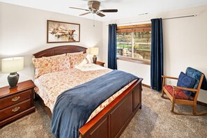 A bedroom with a bed, bedside lamps, a wooden nightstand, a rocking chair, and a window with curtains.