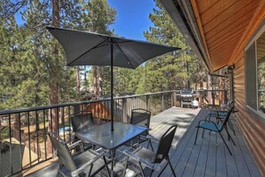 Relax on the elevated deck with a glass-top table and comfortable seating, overlooking the forested landscape.