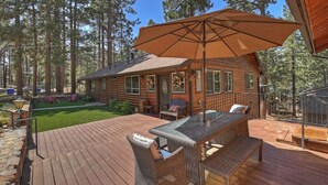 Una cabaña de madera con un porche, mobiliario exterior y un gran parasol.