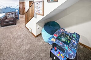 A room with a carpeted floor, a brown leather chair, a blue bean bag, a gaming console, and a wall with a chessboard and a framed picture.