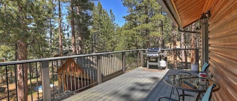 A deck with a grill and chairs, surrounded by trees.