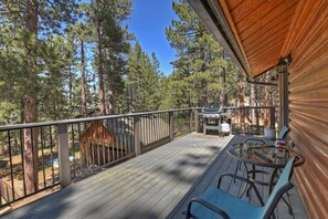 A deck with a grill and chairs, surrounded by trees.