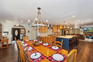 A spacious dining area with a long wooden table set for a meal, a kitchen with wooden cabinets, and a fireplace.