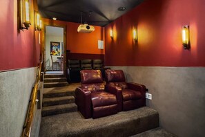 A cinema room with red walls, a projector, and leather recliners.