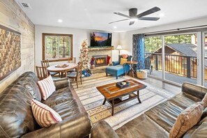 A spacious living room with a fireplace, leather sofas, a coffee table, and a large window overlooking a deck.