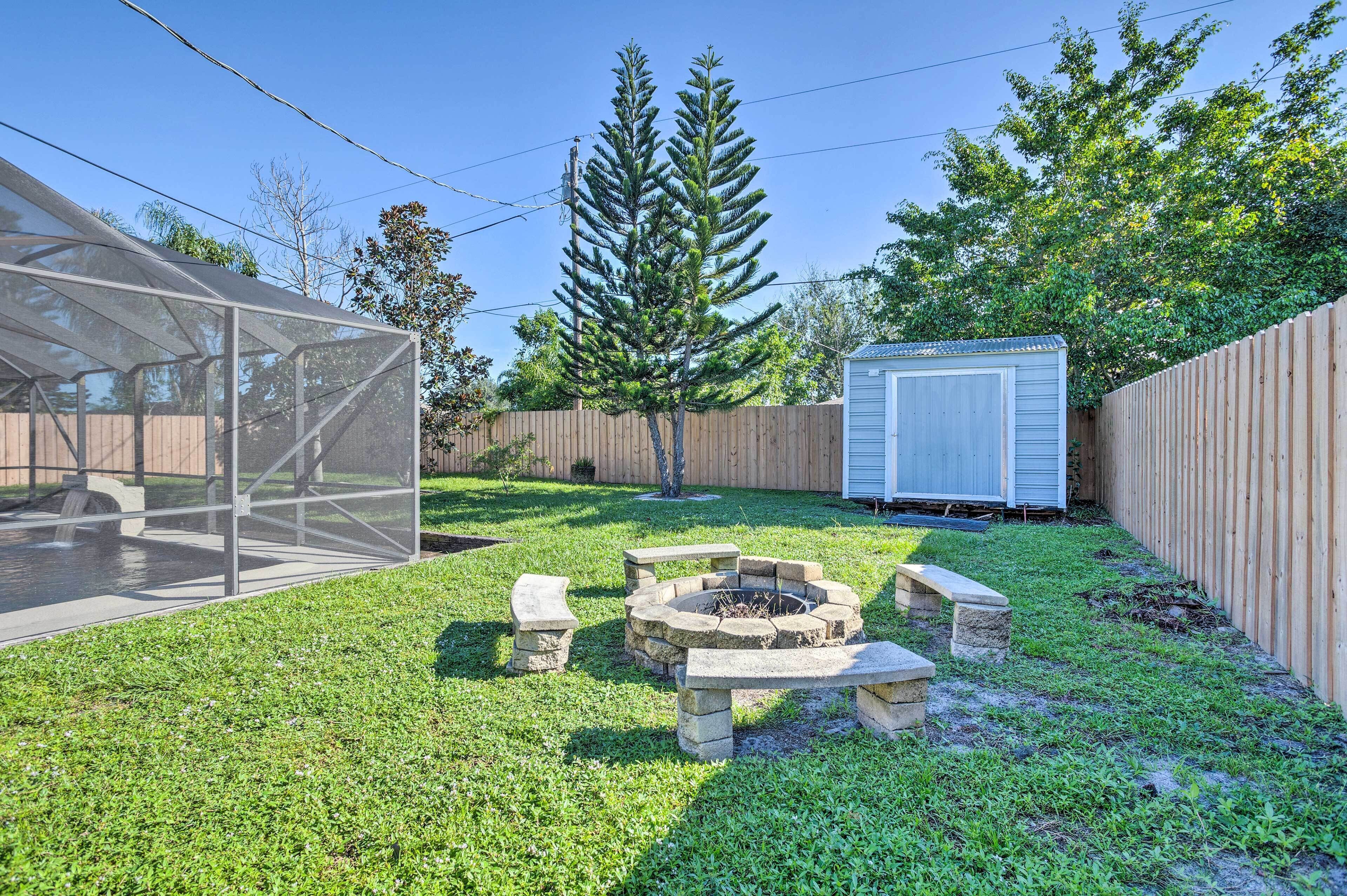 Ein Garten mit Feuerstelle, überdachter Terrasse und Gartenhaus.