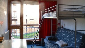 Ein Schlafsaalzimmer mit Etagenbett, einer Schlafcouch, einem Tisch und Blick auf ein Gebäude durch ein Fenster.